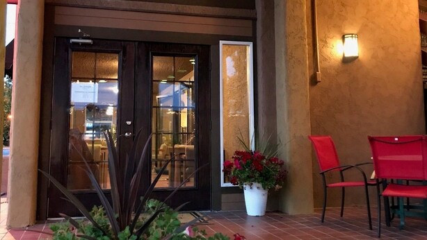 A building entrance with a wooden ceiling, a sign with a bull's head, and a potted plant with red flowers. - Adobe Inn (Durango)