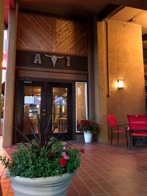 A building entrance with a wooden ceiling, a sign with a bull's head, and a potted plant with red flowers. - Adobe Inn (Durango)