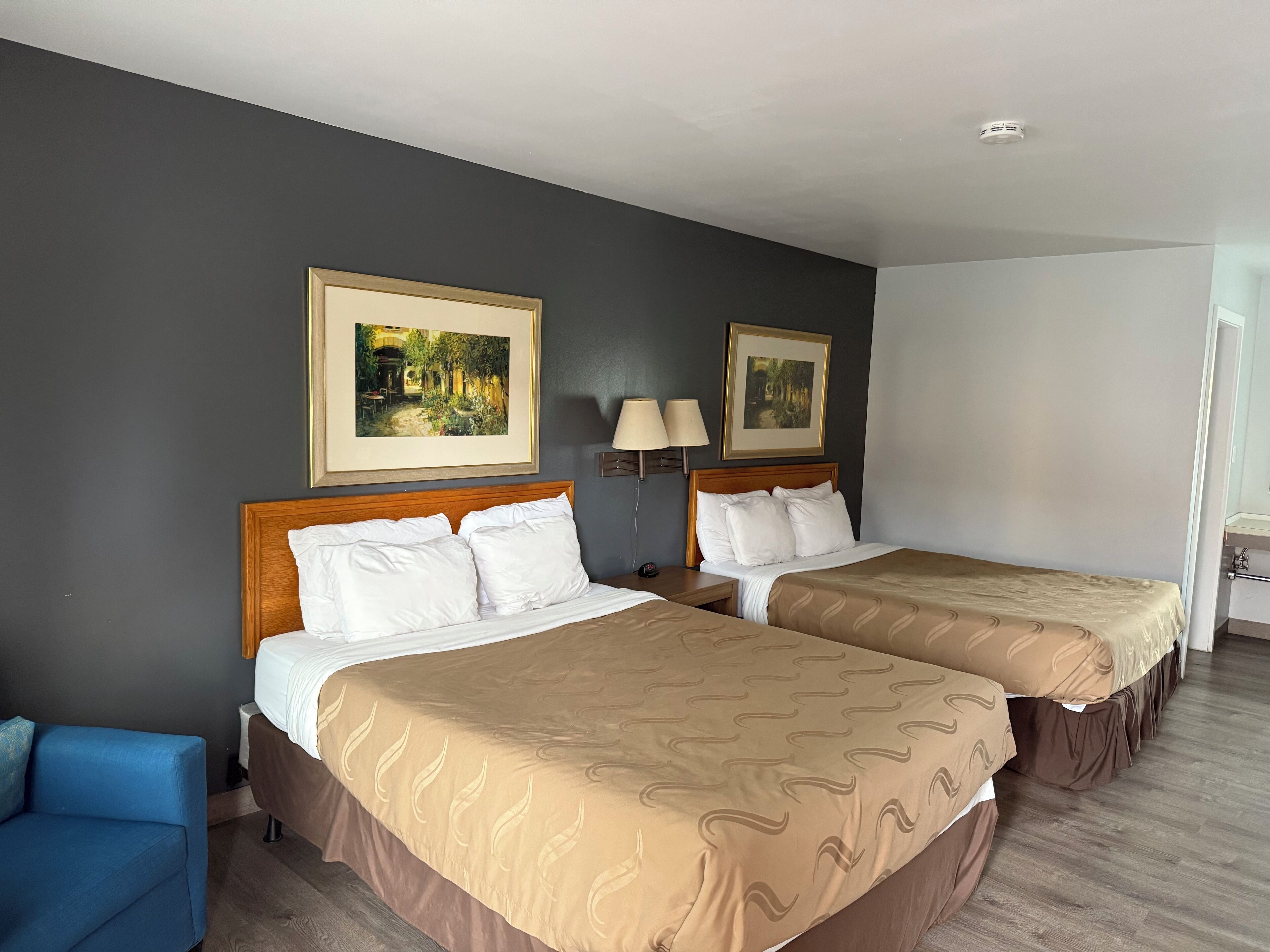 Een hotelkamer met twee bedden, een blauwe stoel en twee schilderijen aan de muur.