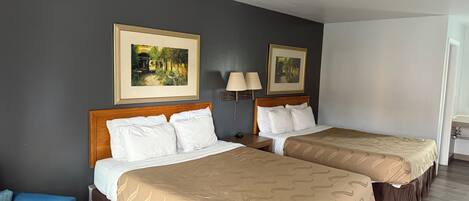 A hotel room with two beds, a blue chair, and two paintings on the wall.