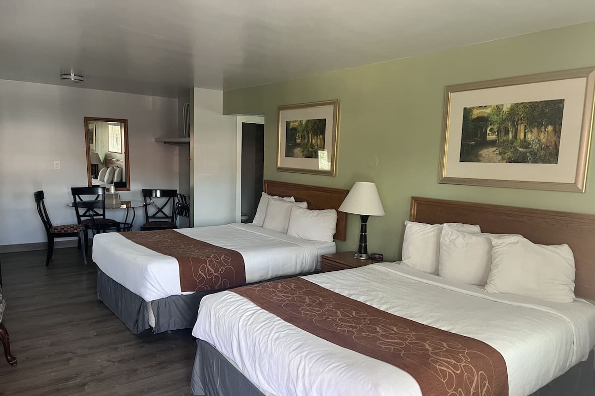 Quarto de hotel com duas camas, uma escrivaninha, cadeiras e obras de arte nas paredes.