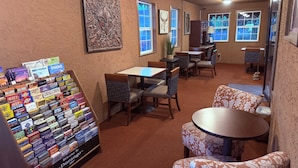 A restaurant with tables and chairs, a display of travel books, and artwork on the walls. - Adobe Inn (Durango)
