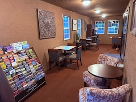 Un restaurante con mesas y sillas, una exhibición de libros de viaje y obras de arte en las paredes.