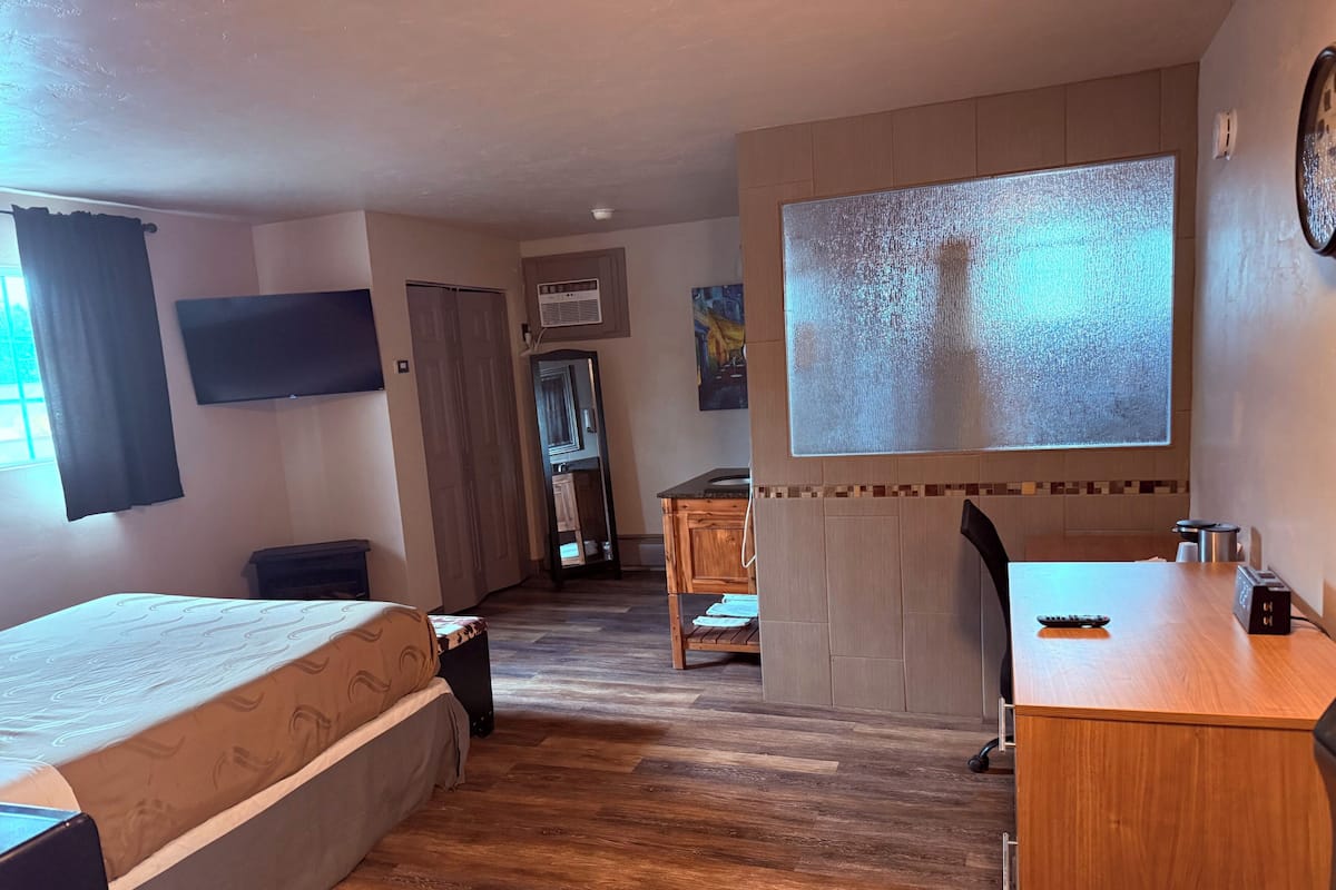 Quarto de hotel com cama, escrivaninha, cadeira, televisão e uma janela grande.