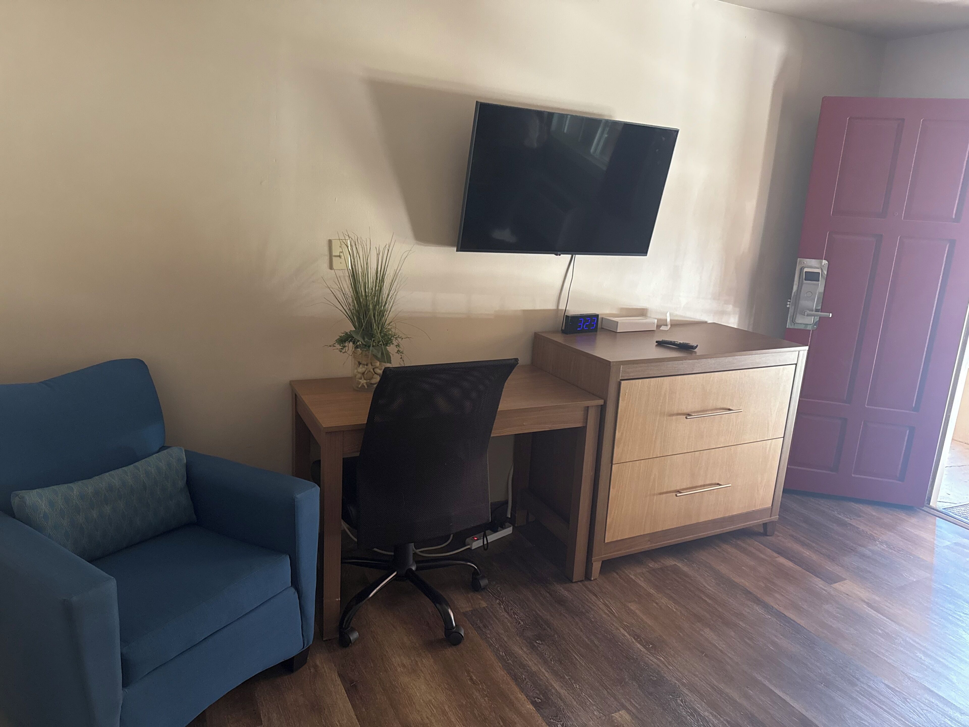 A room with a blue sofa, a wooden desk with a computer, a TV, and a door.