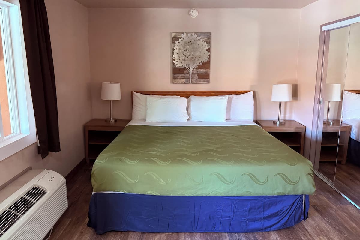 Quarto de hotel com uma cama grande, duas mesas de cabeceira com luminárias, ar condicionado na parede e uma janela com cortinas.