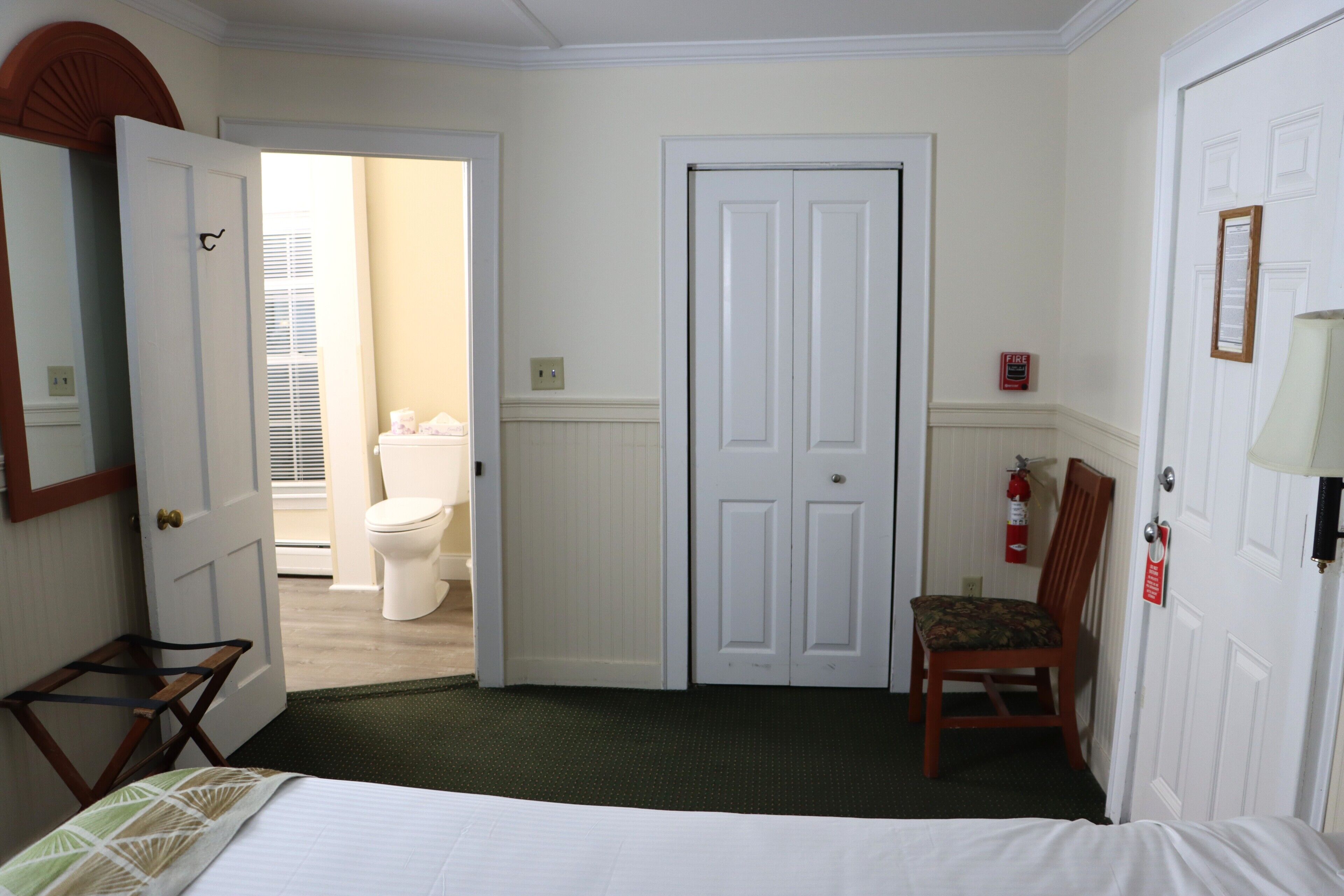 Una habitación de hotel con cama, una silla, una puerta y baño visible.