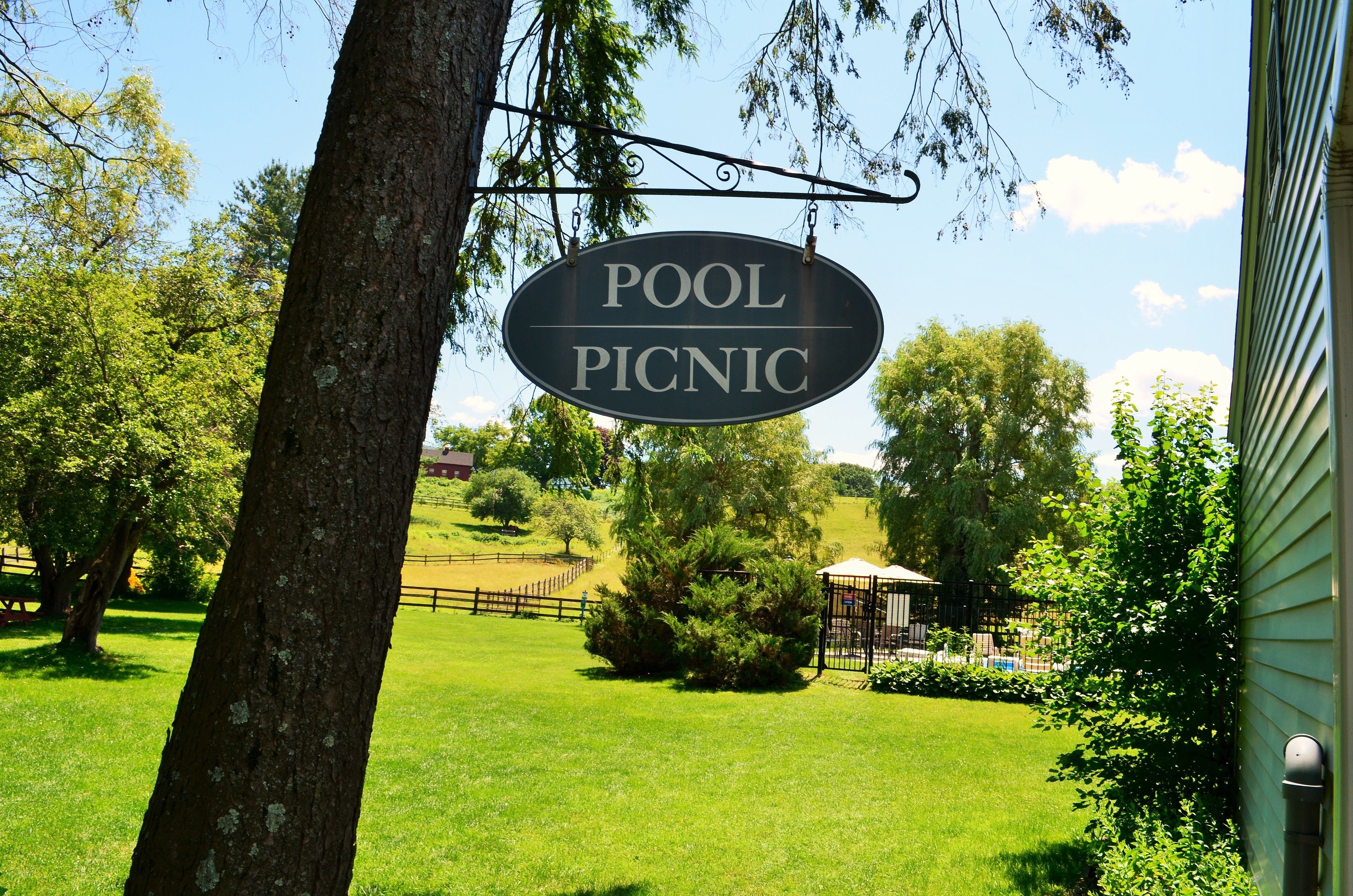 Un panneau indiquant une aire de pique-nique près d’une piscine, avec une pelouse clôturée et des arbres en arrière-plan.