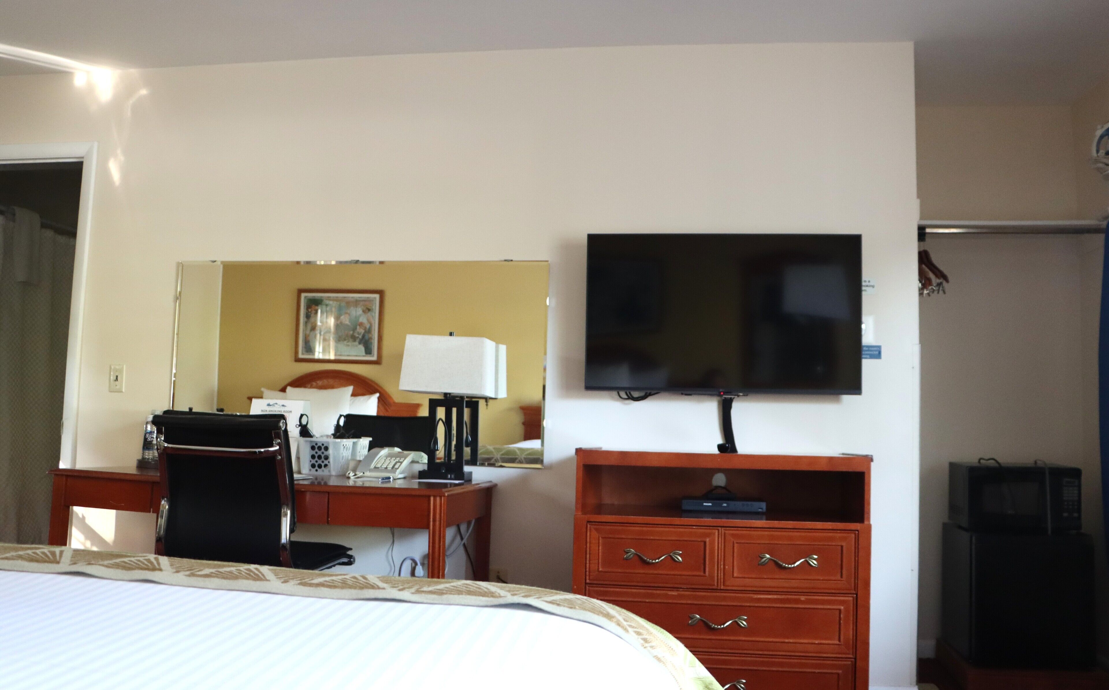 Ein Hotelzimmer mit Bett, Schreibtisch, Stuhl, Fernseher und Kommode.