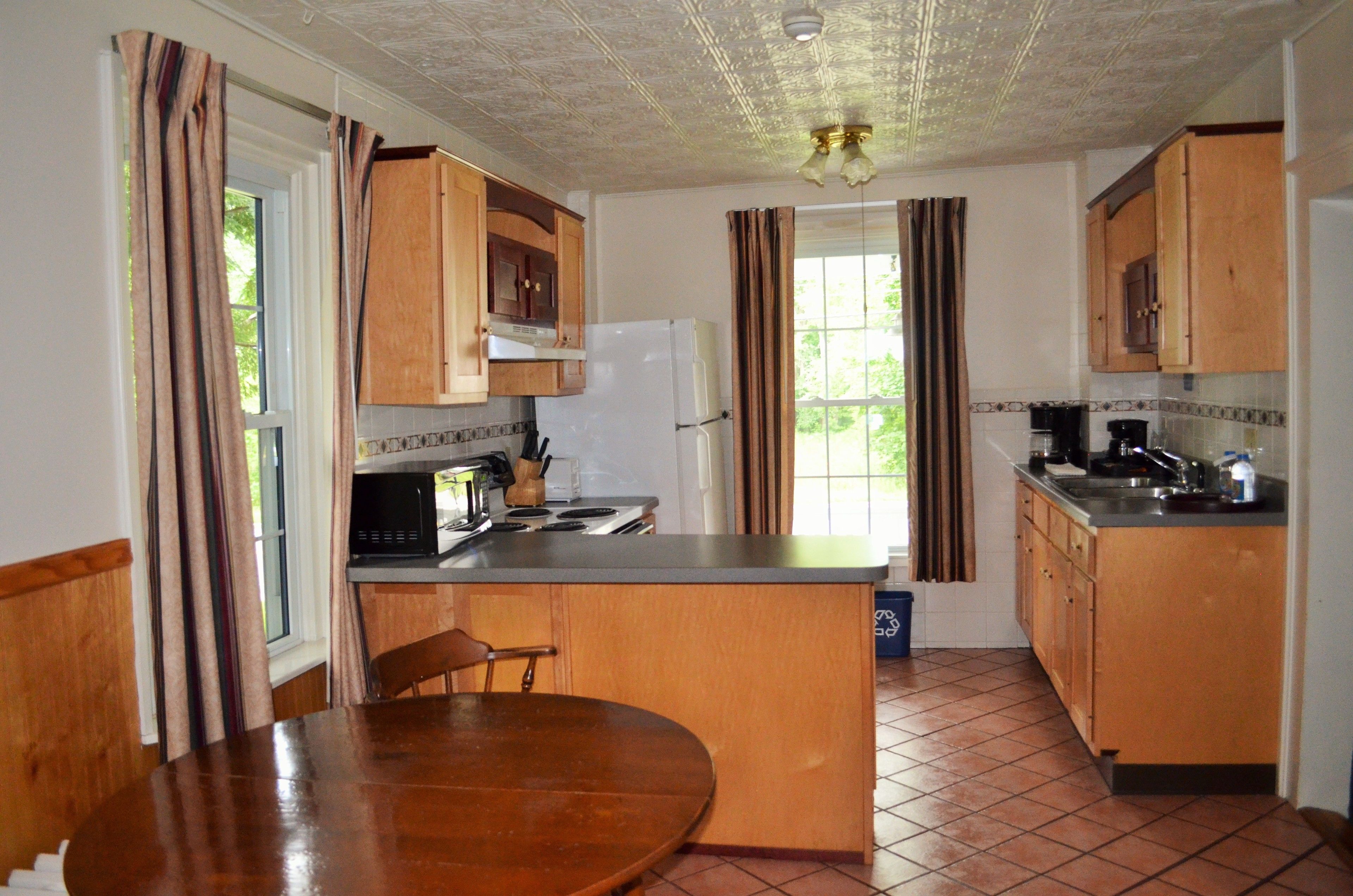 A compact kitchen with wooden cabinets, a refrigerator, a microwave, and a sink.