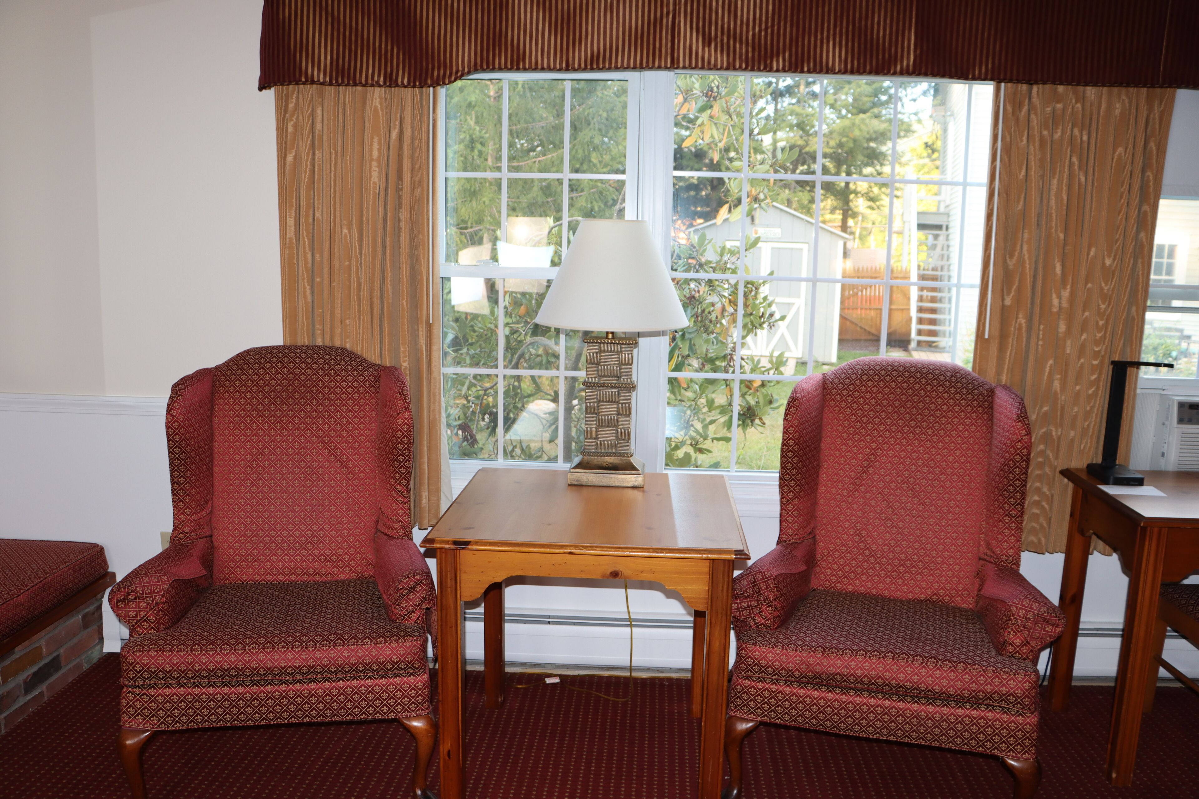 A room with two patterned armchairs, a wooden table, and a lamp.