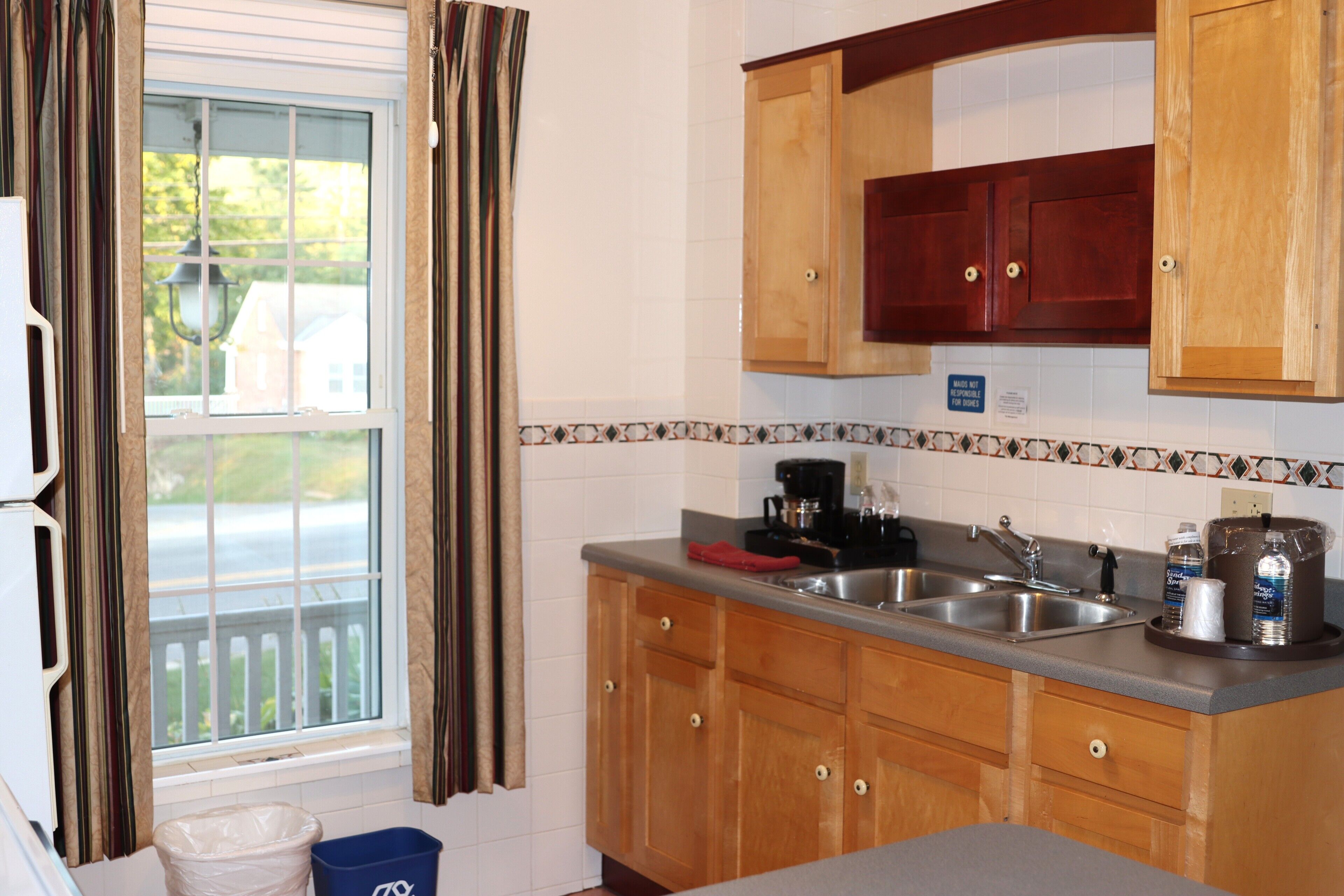 A kitchen with wooden cabinets, a double sink, and a window with curtains.