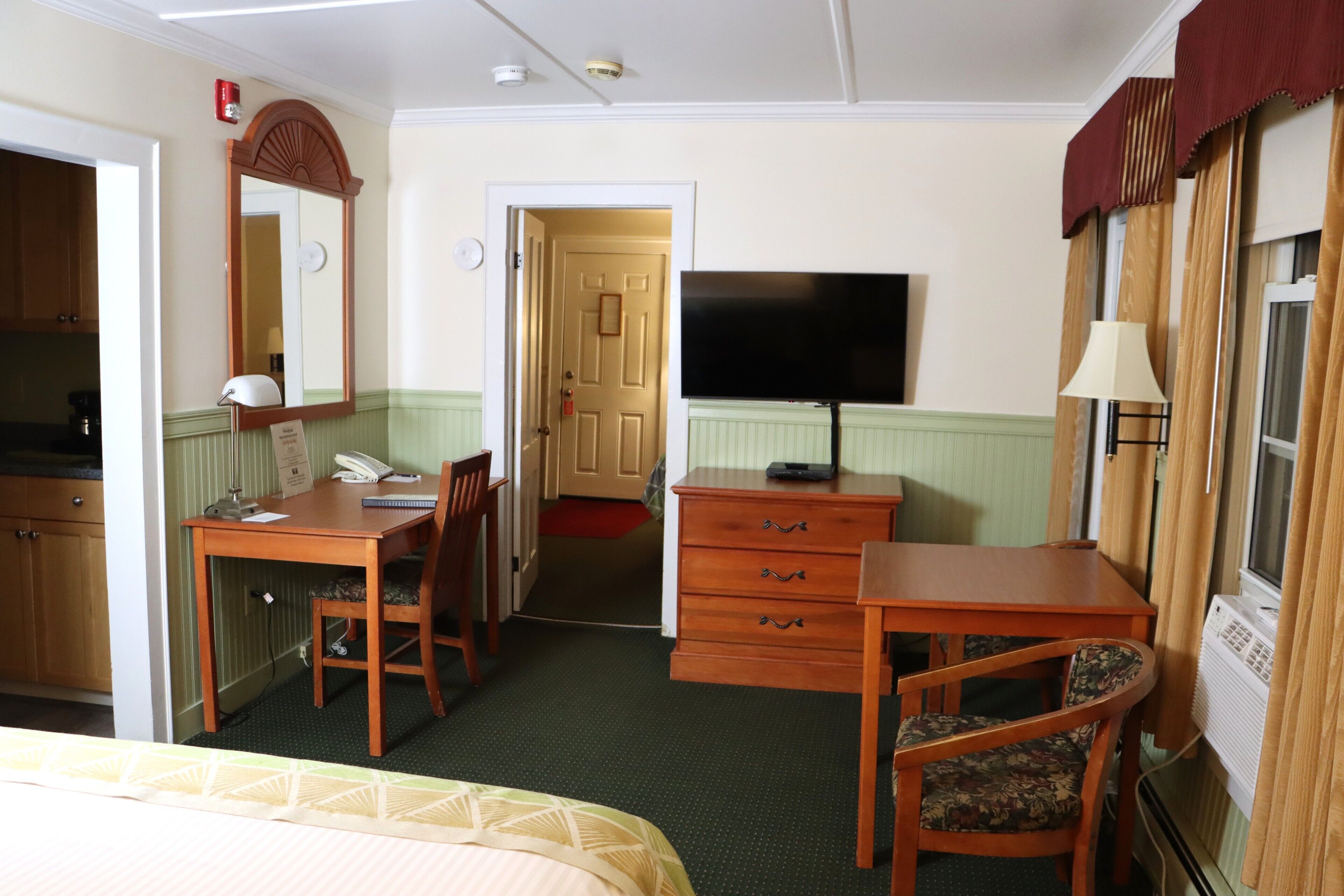 Habitación de hotel con cama, escritorio, silla, cómoda, televisor y ventana con cortinas.