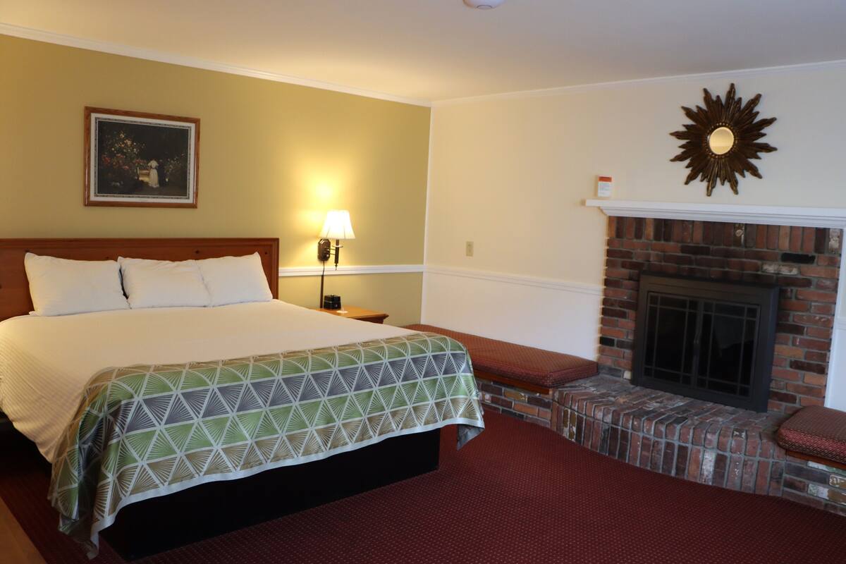 Une chambre d’hôtel avec un grand lit, une cheminée, une table de chevet et une lampe fixée au mur.