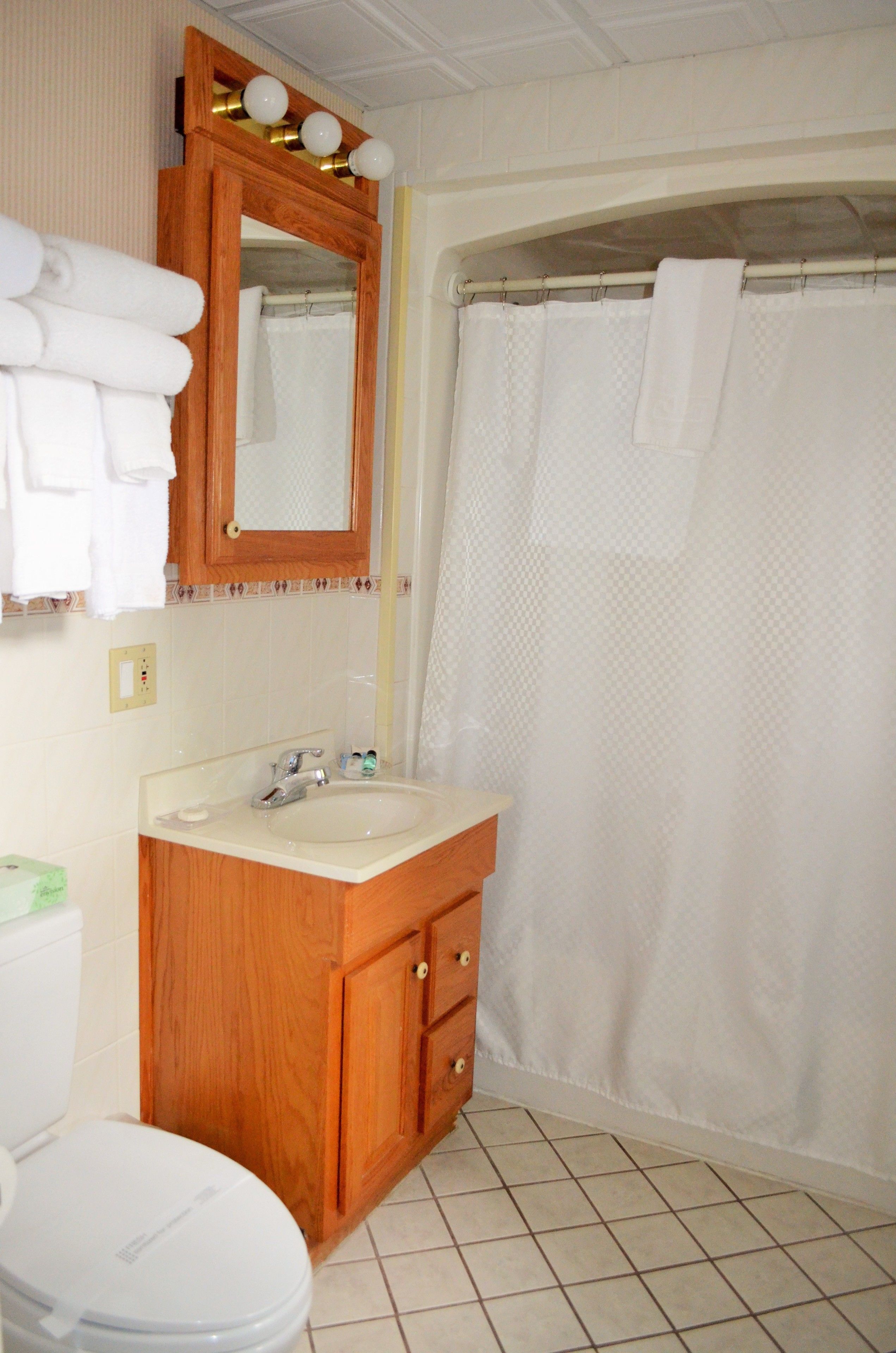 Un baño con tocador de madera, lavamanos blanco, espejo, inodoro y cortina de ducha.