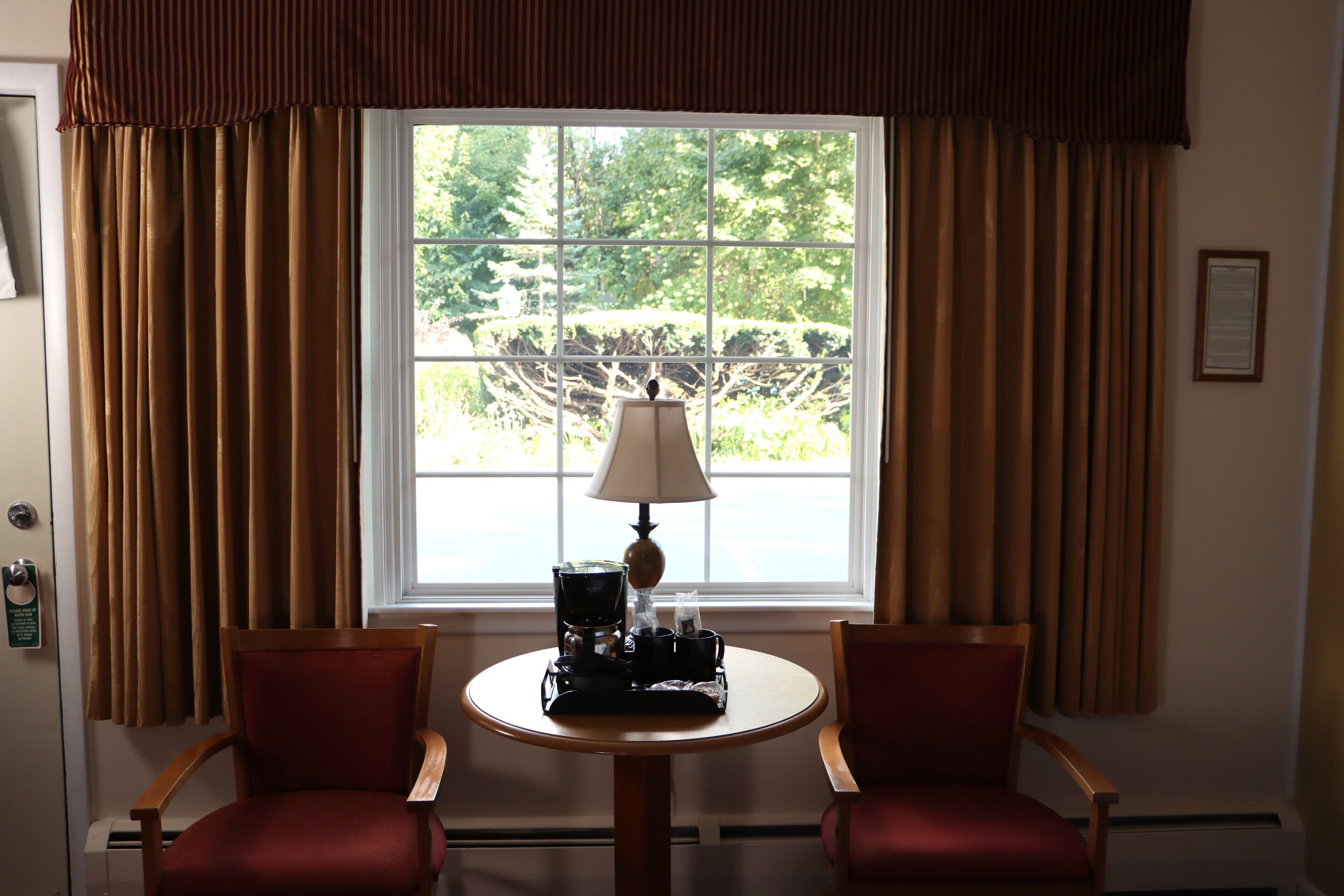 A room with a window, two chairs, a table with a lamp, and a coffee maker.