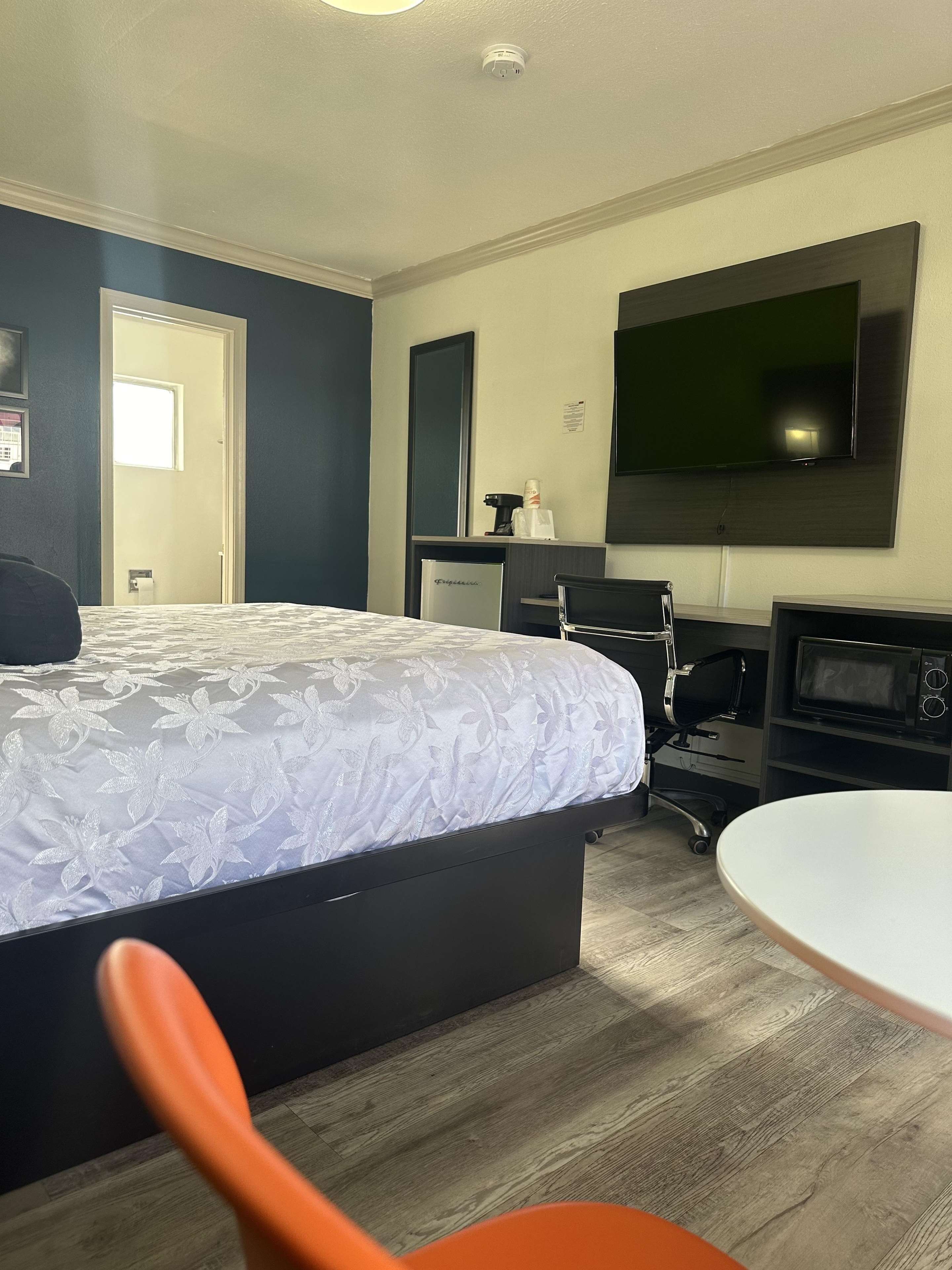 A hotel room with a bed, a desk, a chair, a TV, and a microwave.