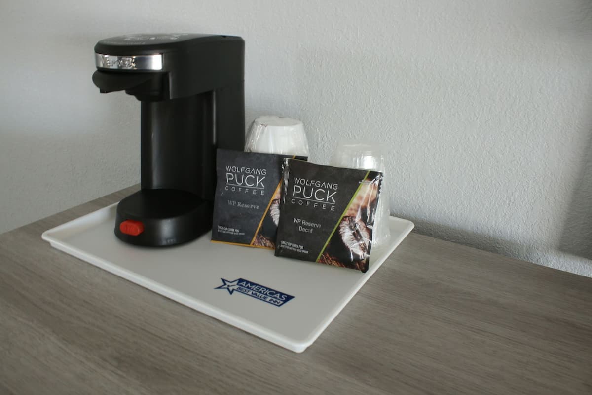 A coffee maker, two packets of coffee, and a disposable cup on a tray.