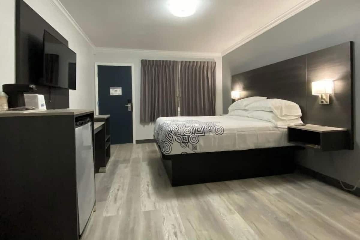 A hotel room with a bed, a TV, a desk, and a door.