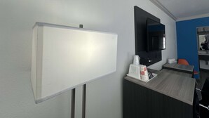 Une chambre d’hôtel équipée d’un tableau blanc, d’un téléviseur à écran plat fixé au mur, d’un bureau en bois avec un plateau contenant des articles de toilette et d’un miroir qui reflète la pièce.