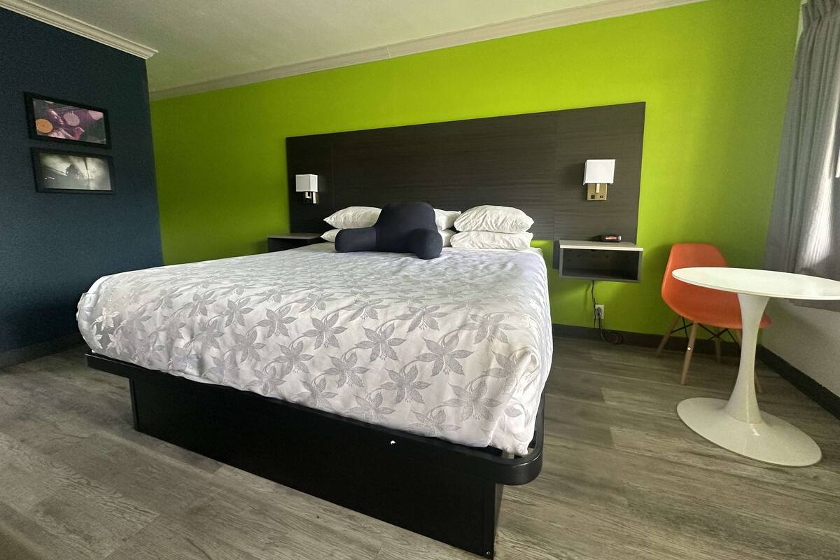 A hotel room with a bed, a desk, a chair, and a small table.