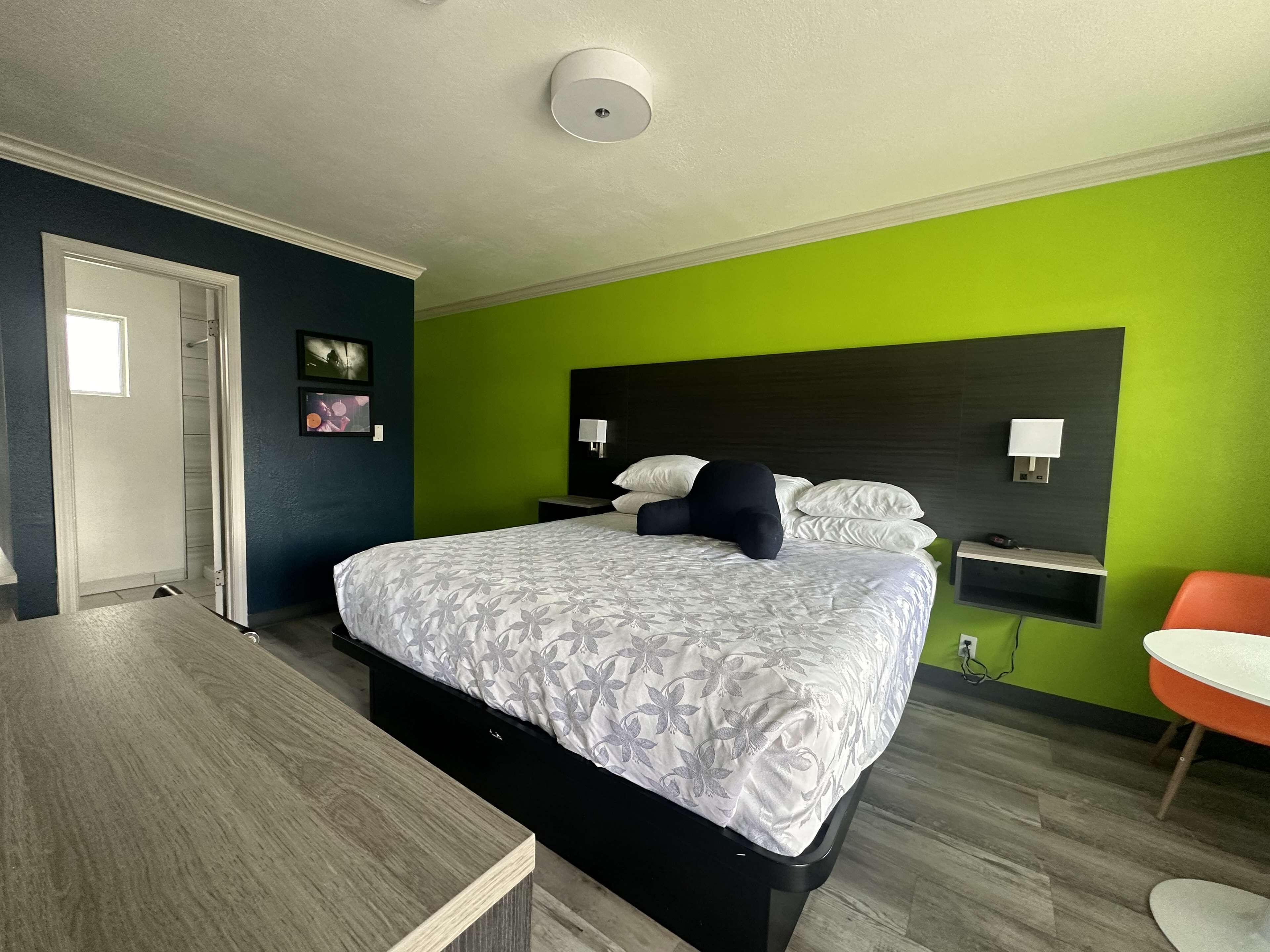 Una habitación de hotel con cama, mesitas de noche, escritorio, una silla y una lámpara de pared.