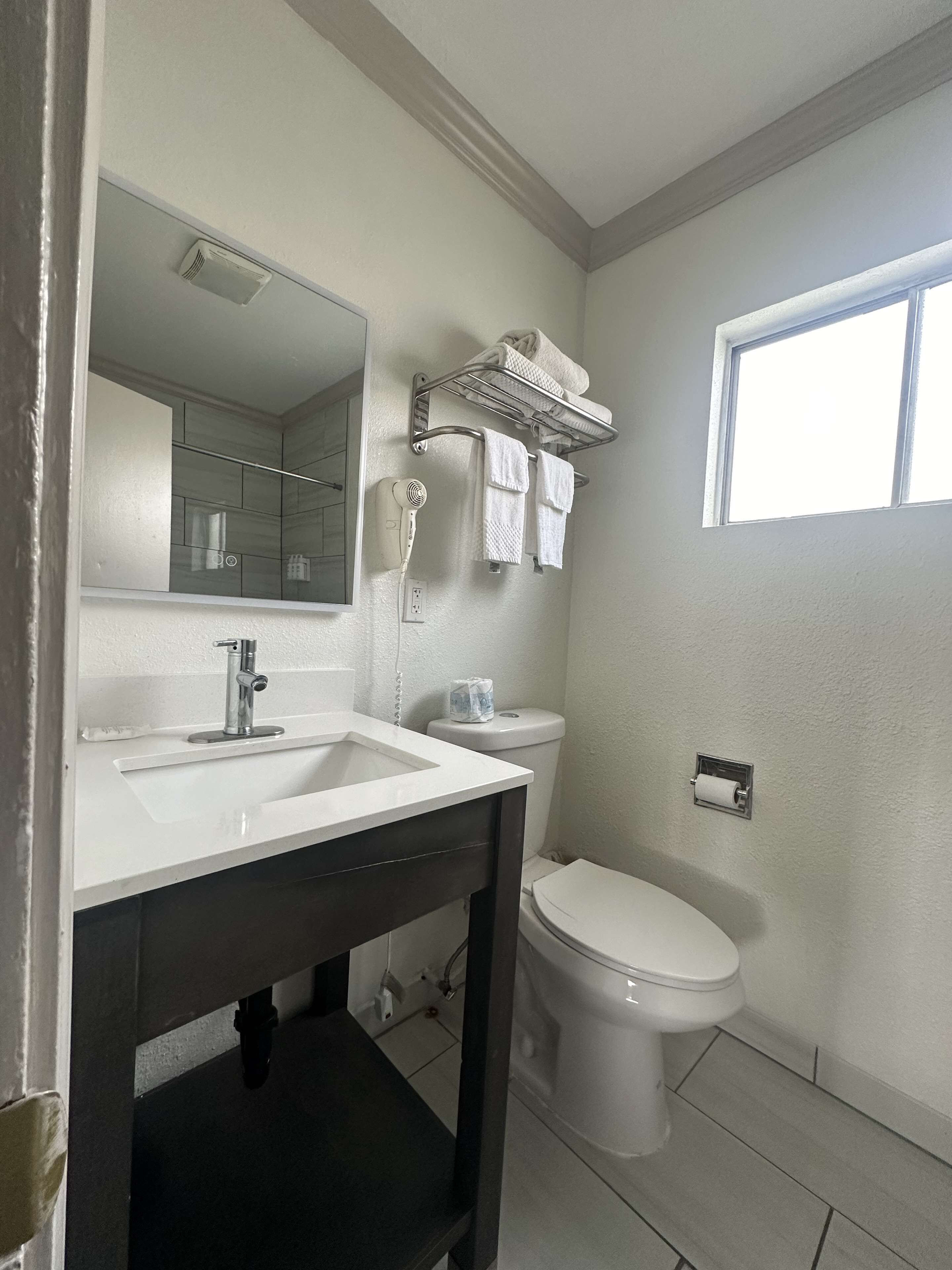 A bathroom with a white sink, a mirror, a towel rack, a toilet, and a window.
