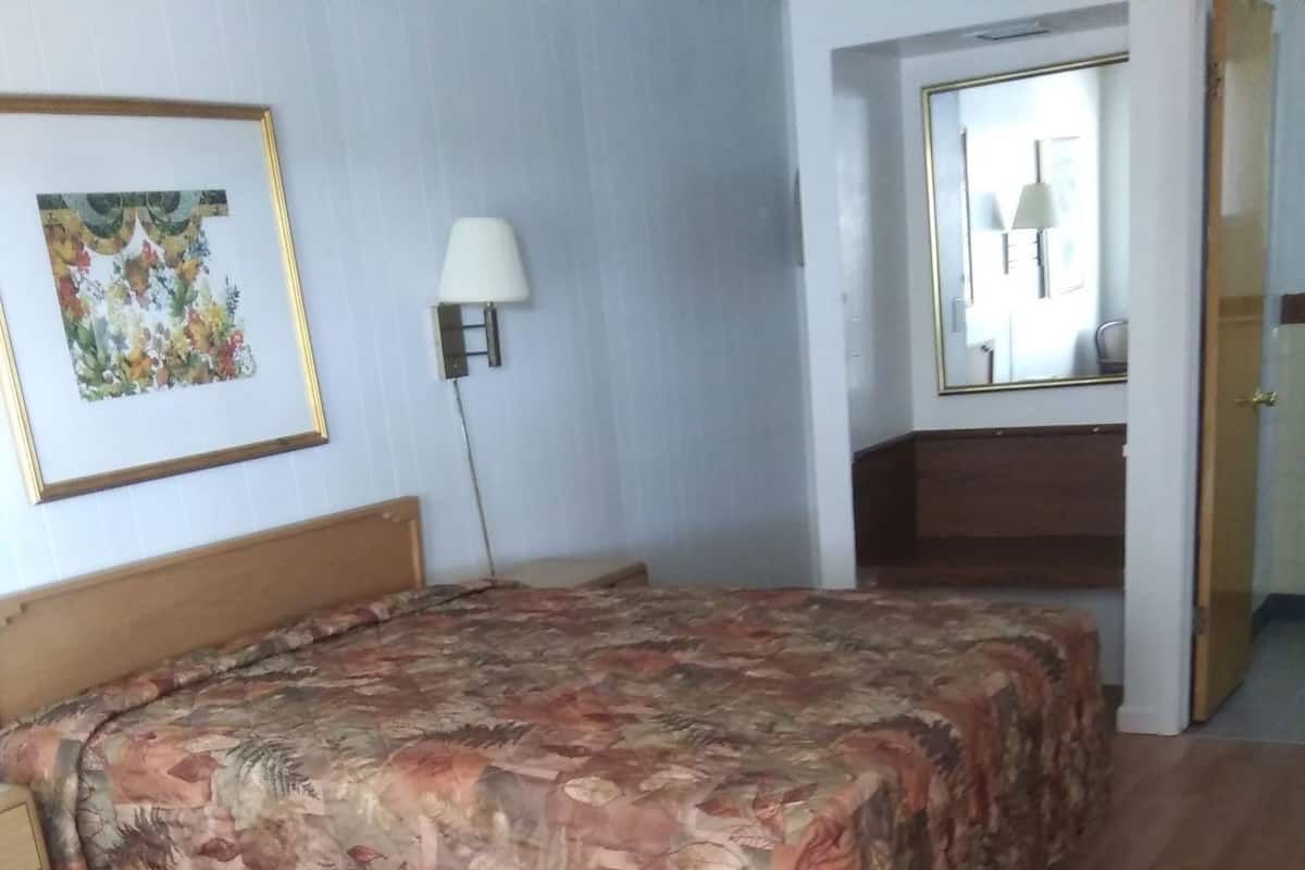 A bedroom with a floral bedspread, a bedside lamp, a wooden headboard, and a wooden floor.