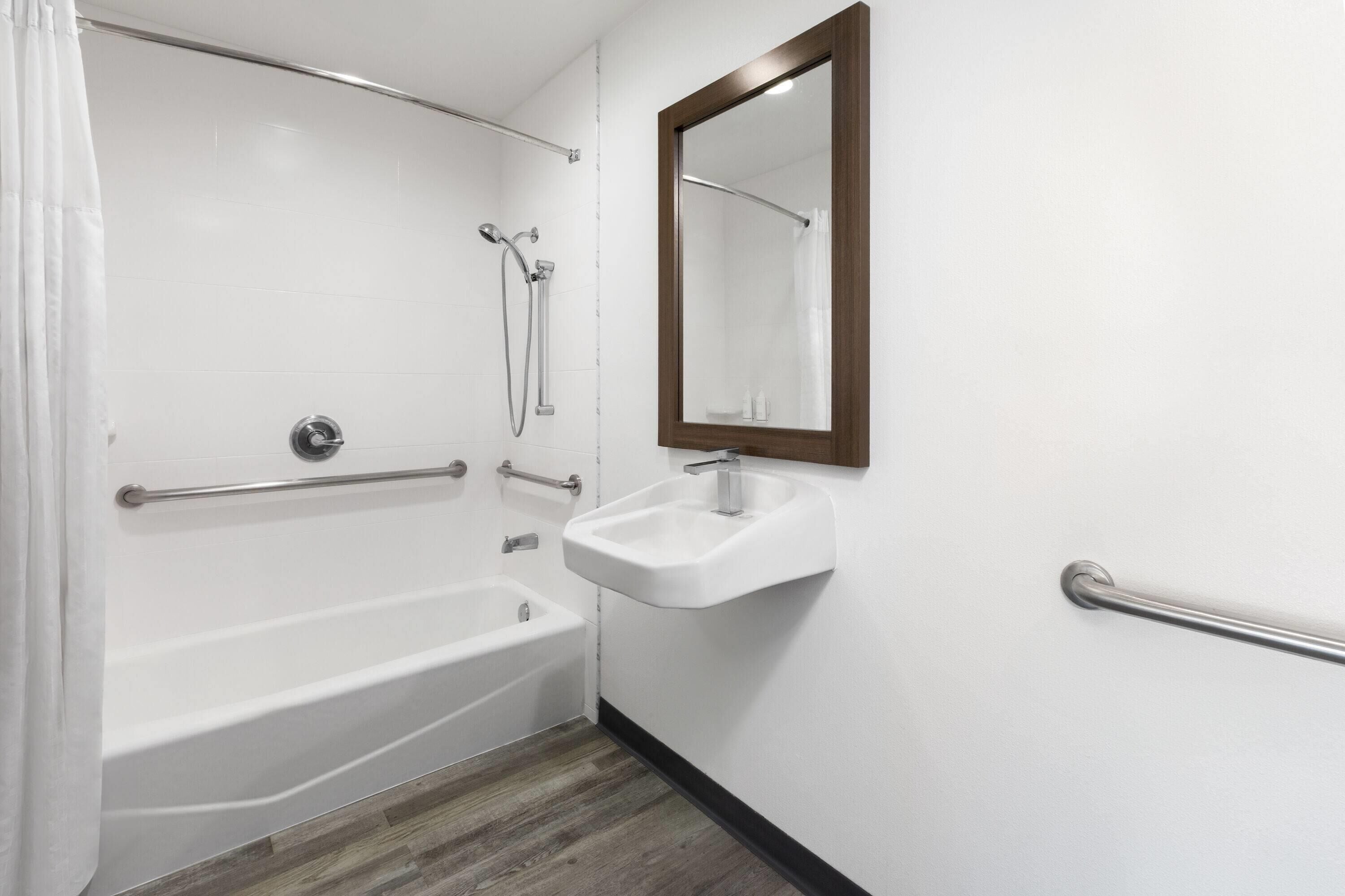 A bathroom with a white bathtub, a sink with a mirror, and a shower area.