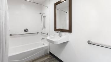A bathroom with a white bathtub, a sink with a mirror, and a shower area.