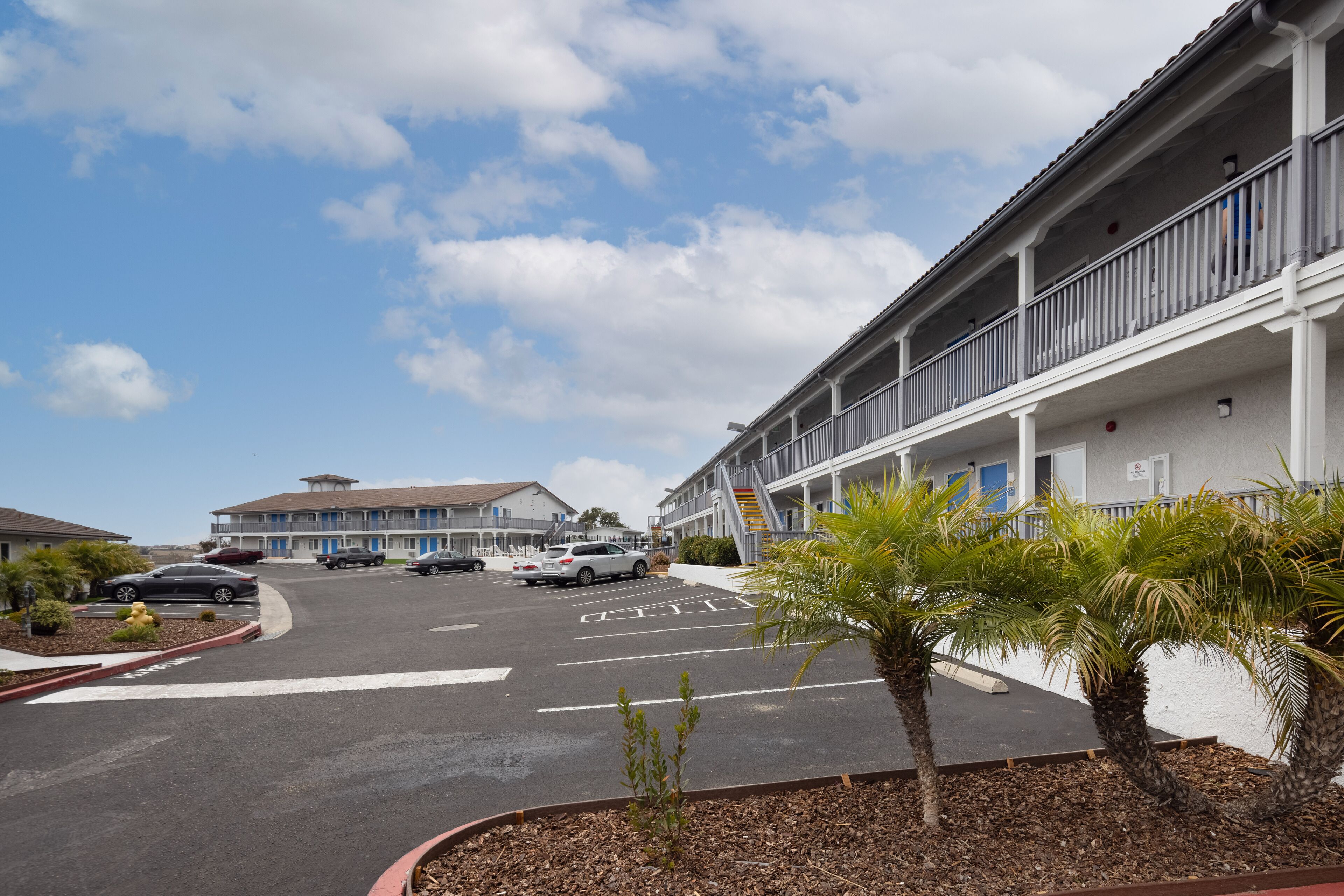 Un motel con estacionamiento, una galería techada y una palmera.