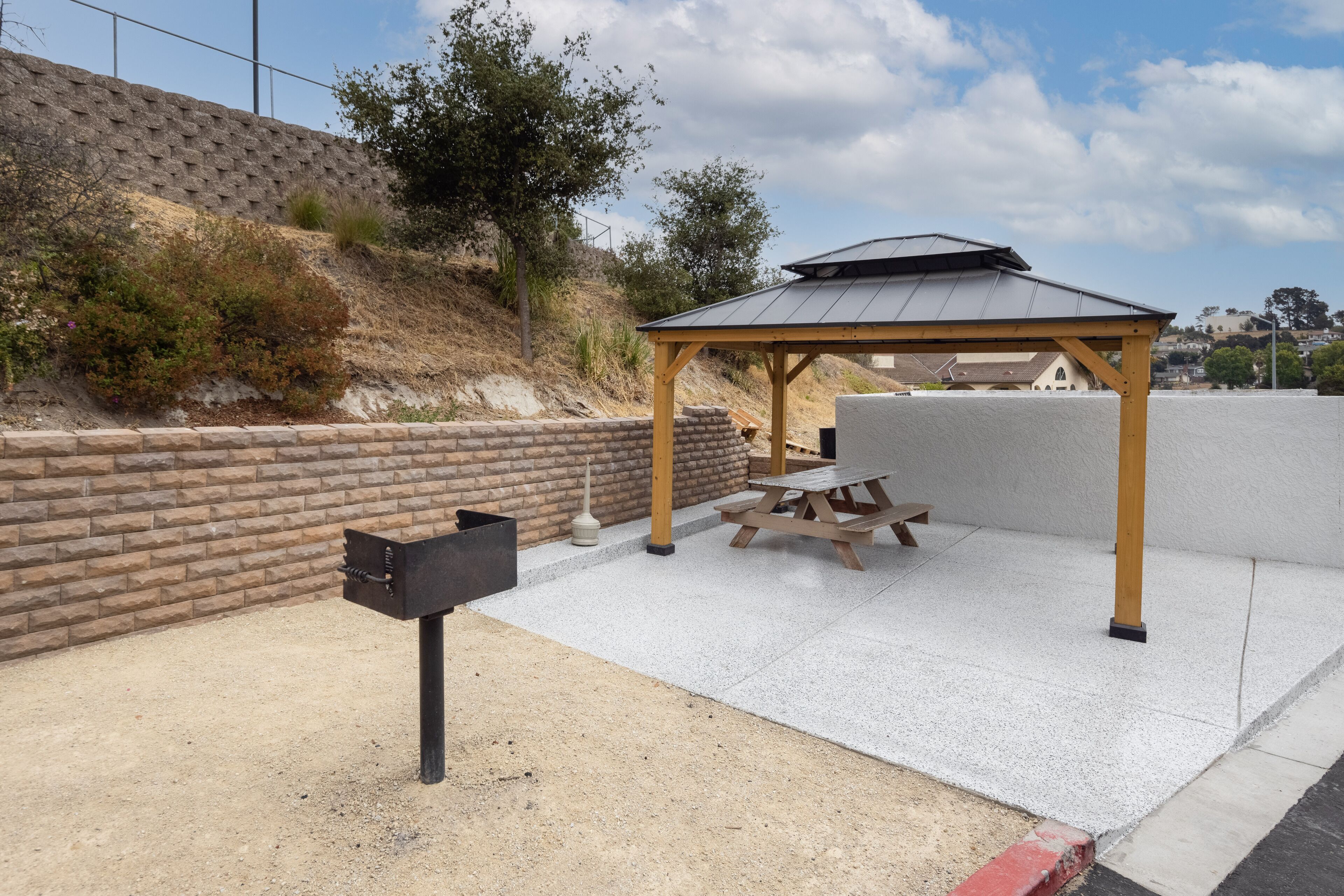 Een overdekt terras met een picknicktafel en banken, een brievenbus, en een bakstenen muur op de achtergrond.