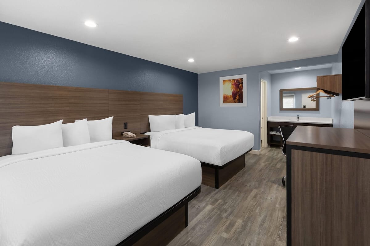 A hotel room with two beds, a desk, a mirror, and a TV.