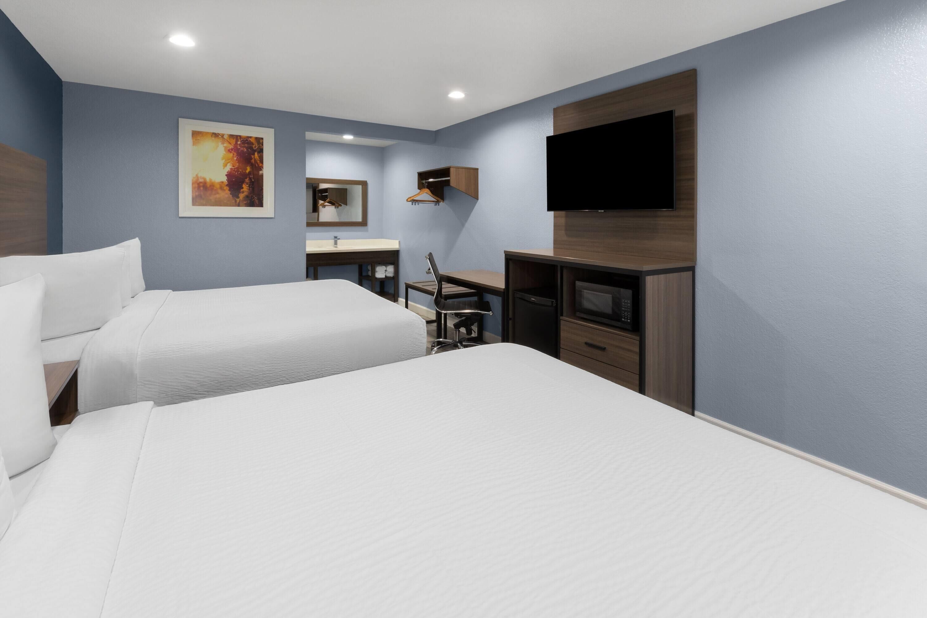 A hotel room with two beds, a desk, a chair, a TV, and a painting on the wall.
