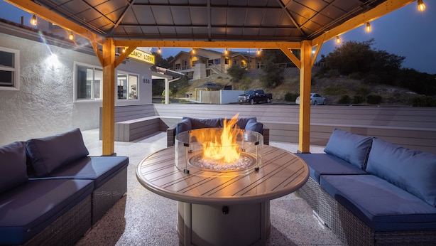 Een terras buiten met een ronde tafel en zitplaatsen, een vuurkorf en een overdekt gedeelte met lichtjes.