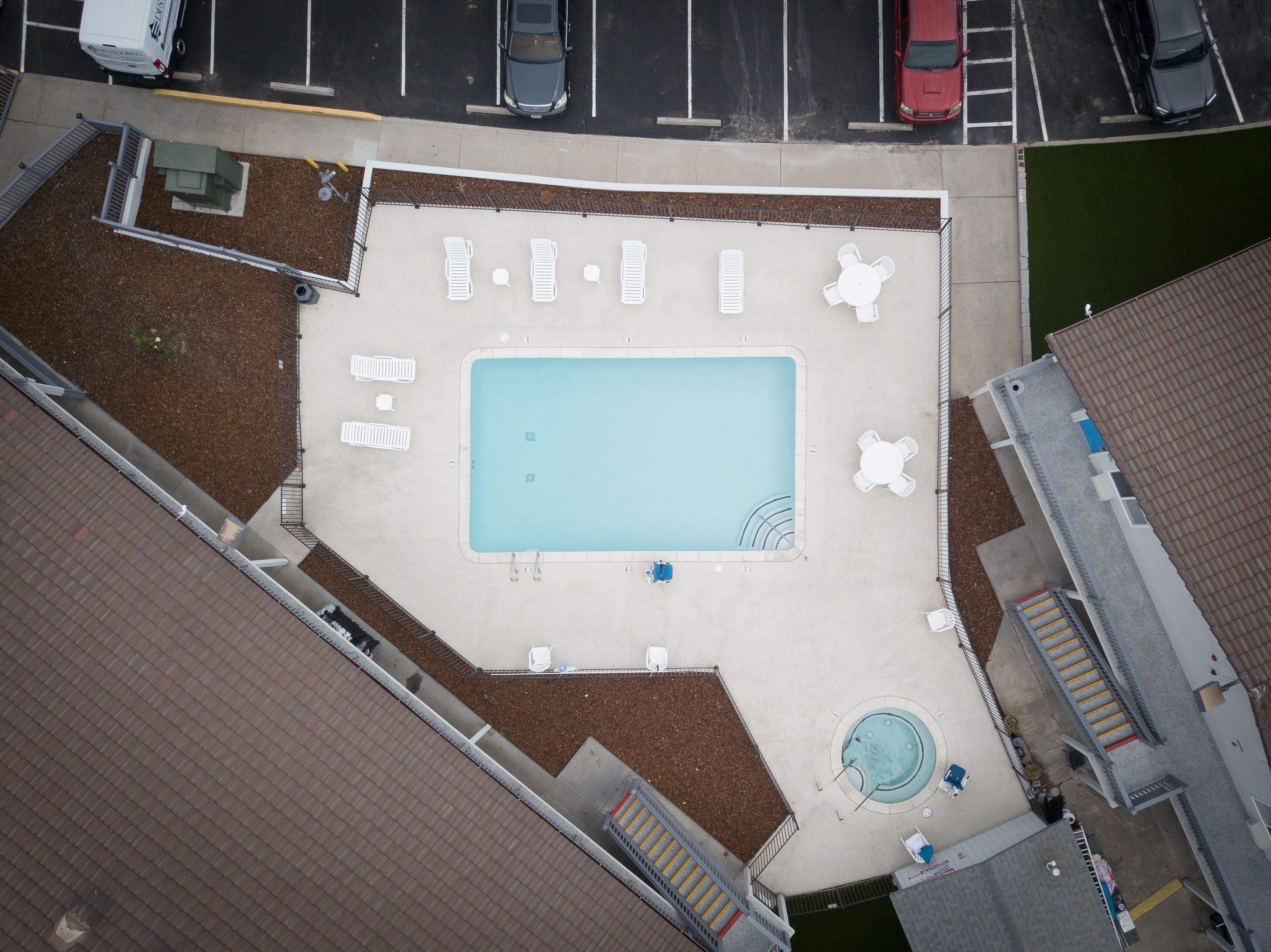 An aerial view of a swimming pool area with multiple lounge chairs, a hot tub, and a small garden area.