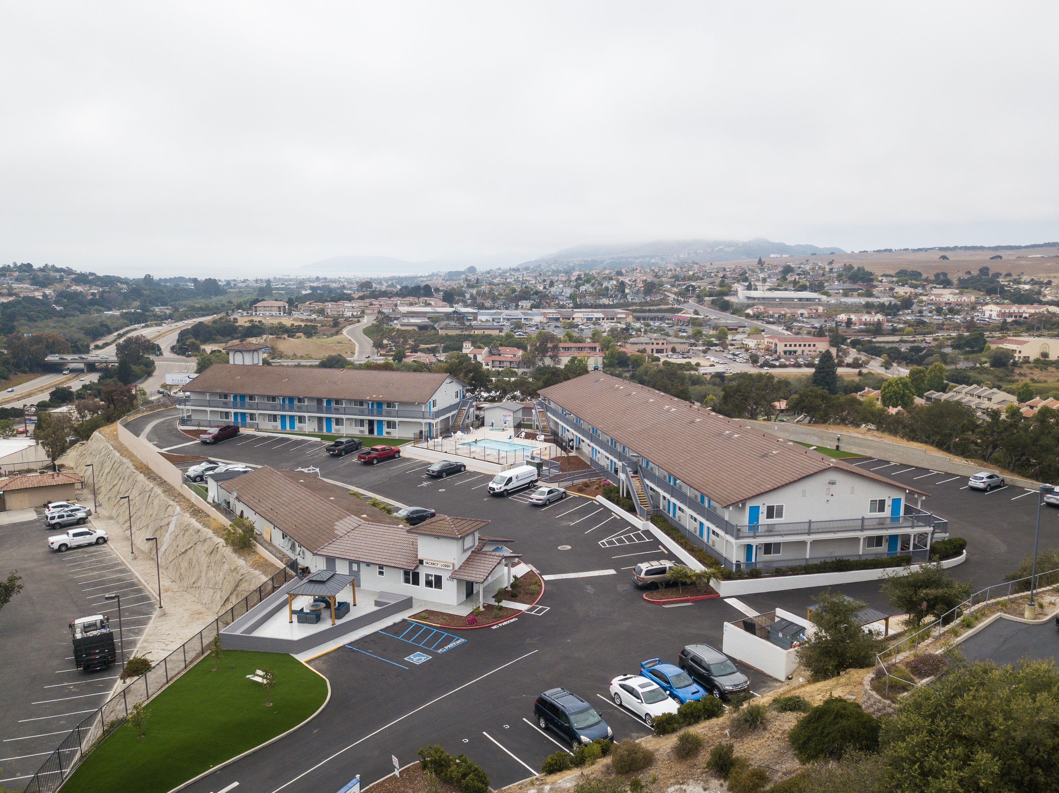 A motel with a parking lot, a swimming pool, and a view of the surrounding town.