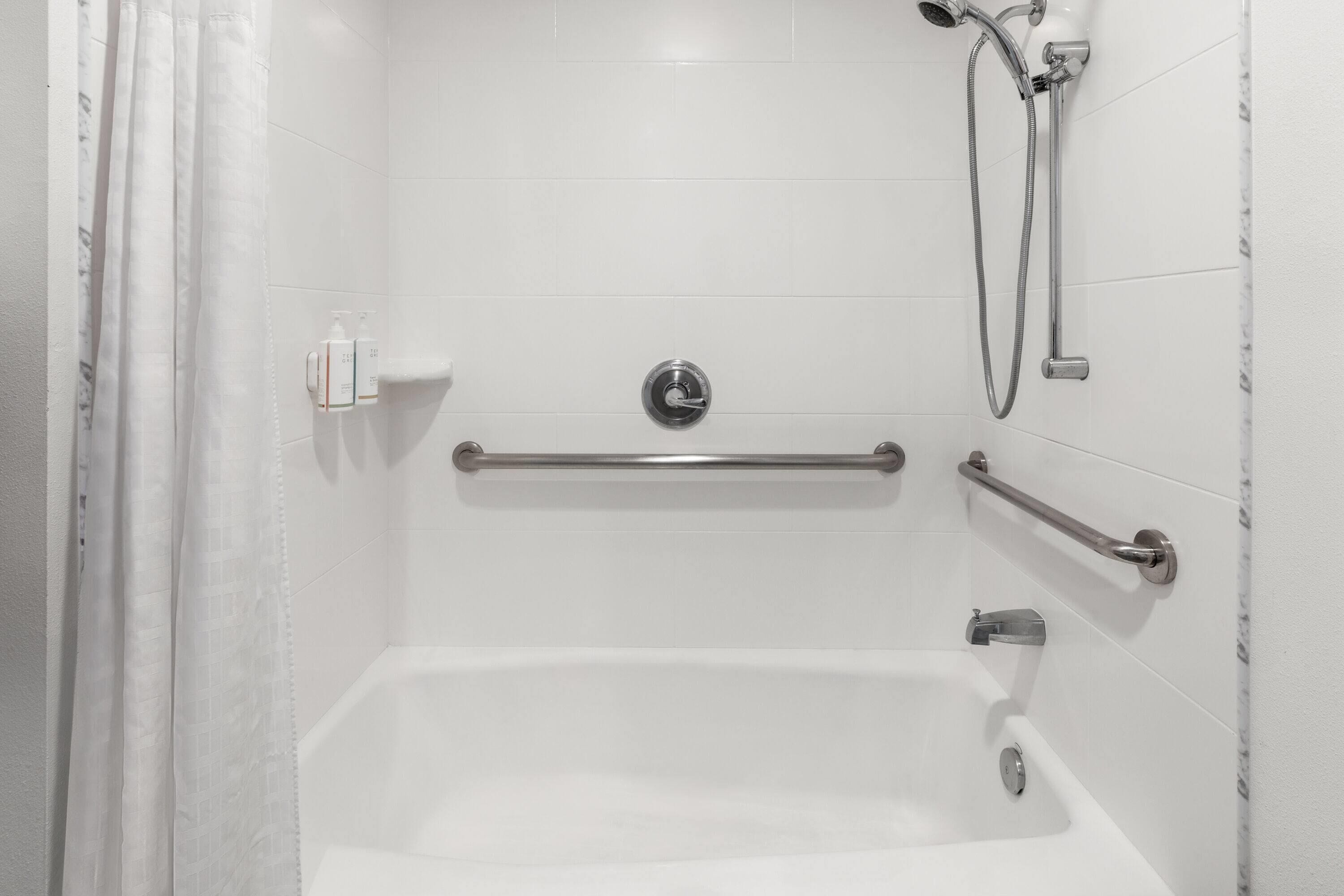 Une salle de bain moderne avec une baignoire blanche, des barres d’appui et une pomme de douche.