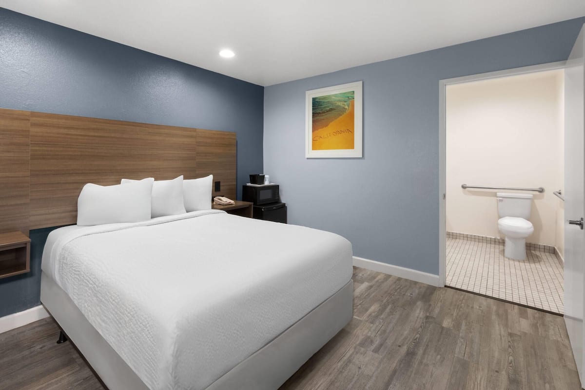 A modern bedroom with a large bed, a wooden headboard, a framed picture on the wall, and a bathroom with a toilet and sink.