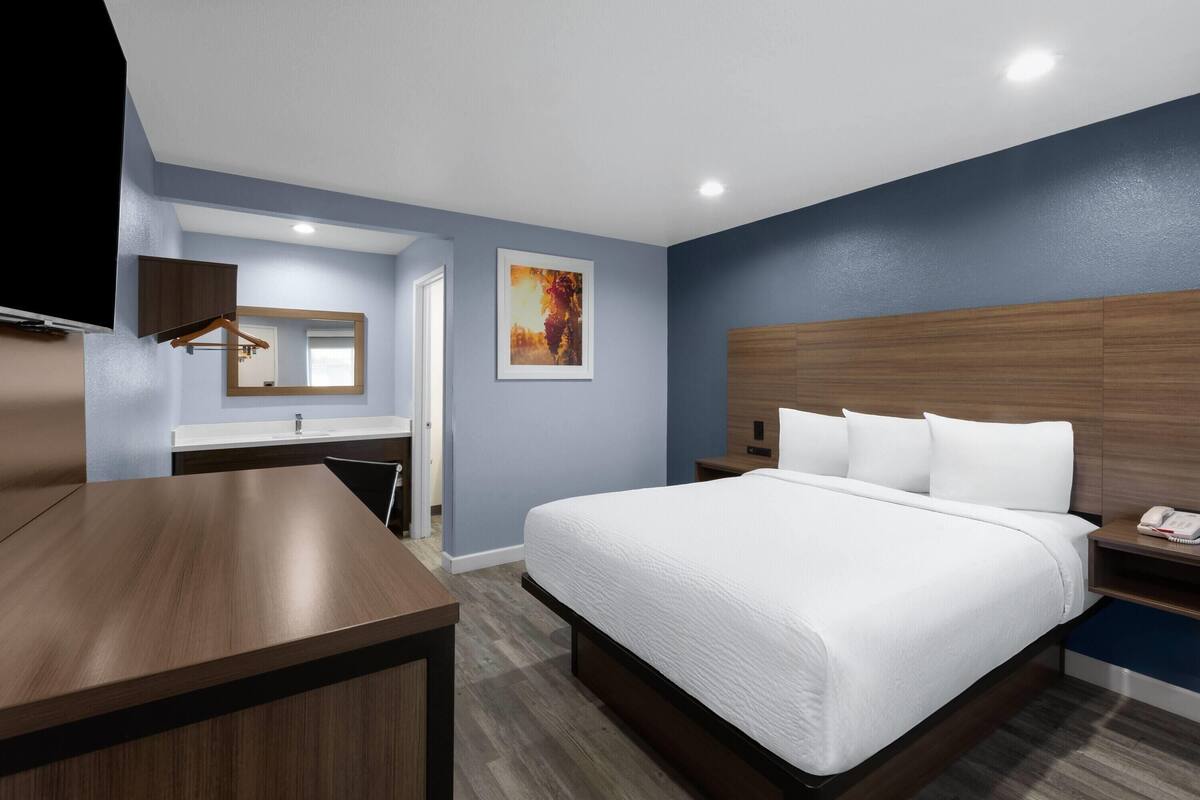 A hotel room with a bed, bedside table, nightstand, and a mounted TV.
