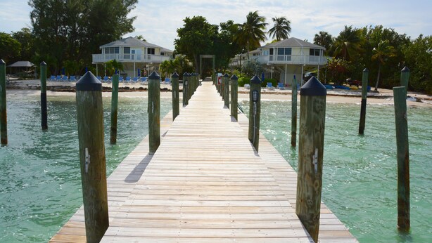 Un muelle de madera que da a una playa con dos casas a cada lado.