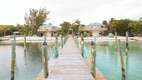 A wooden pier leading to a beachfront property with a pool, lounge chairs, and a covered area. - Topsider Resort (Islamorada)
