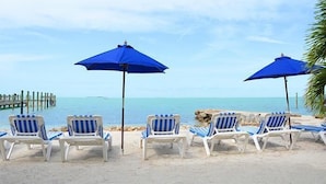 Una playa con sombrillas azules y sillas de playa a rayas frente al océano.