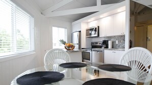 Cocina moderna con armarios blancos, microondas y cafetera. Hay una mesa de comedor con cuatro sillas y un frutero sobre la encimera.