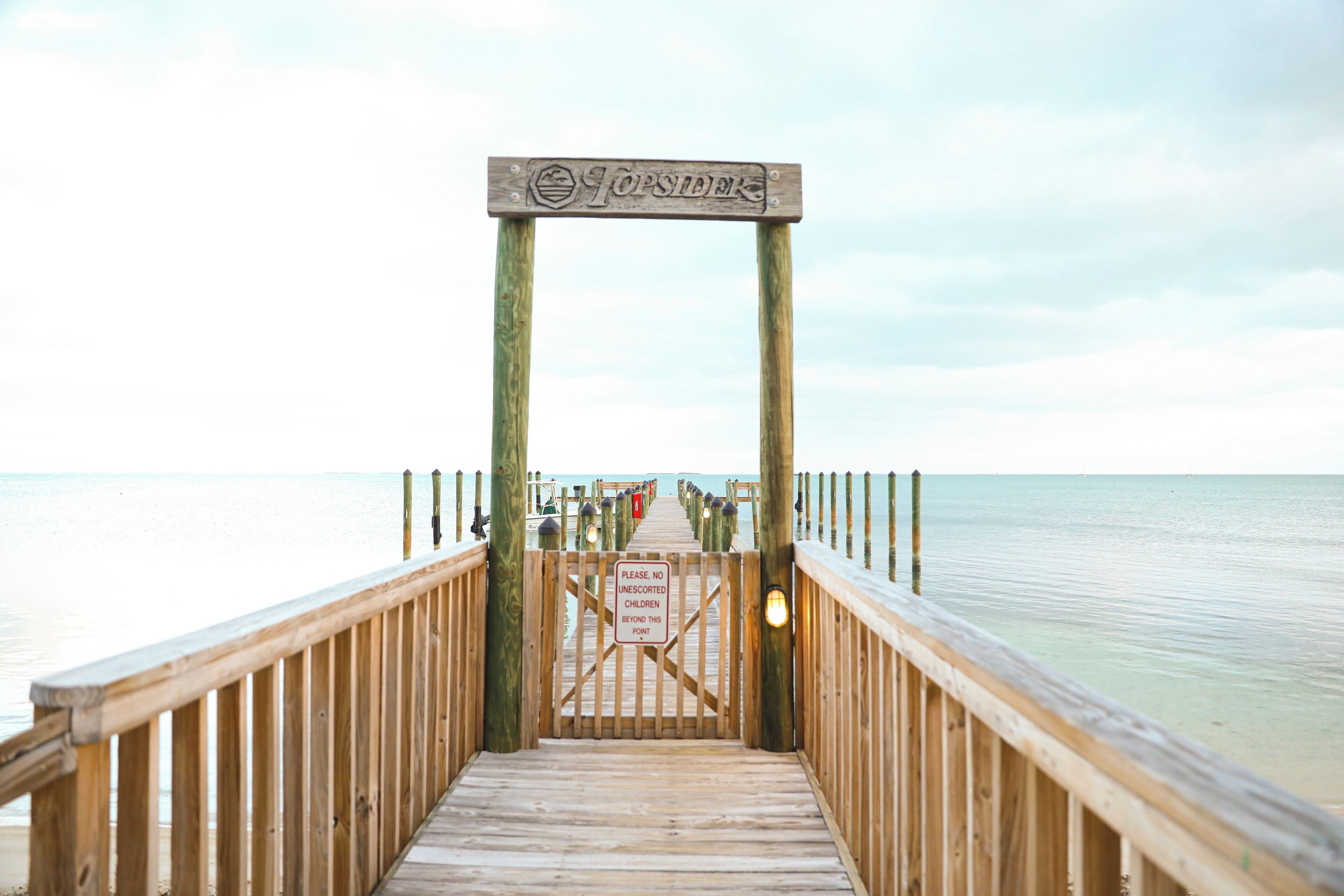 A wooden pier leading to a beach with a sign that reads "TOPSIDEK."
