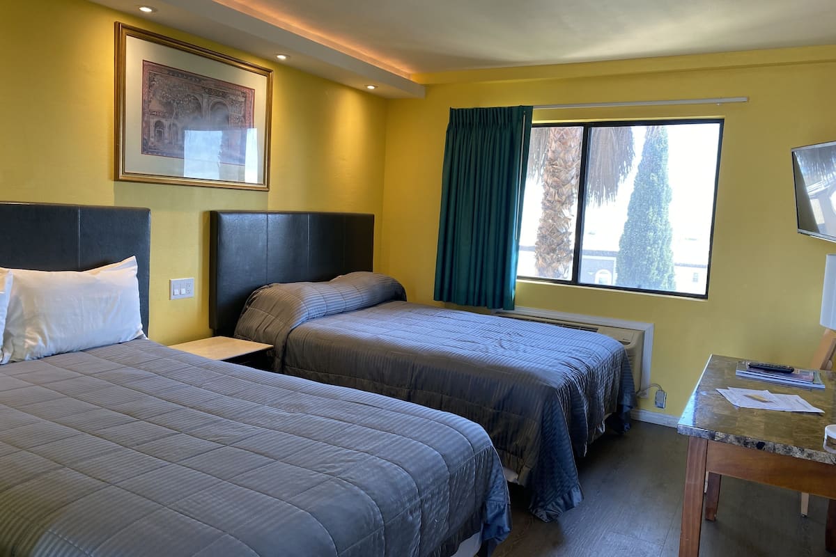 A hotel room with two beds, a desk, a TV, and a window with curtains.