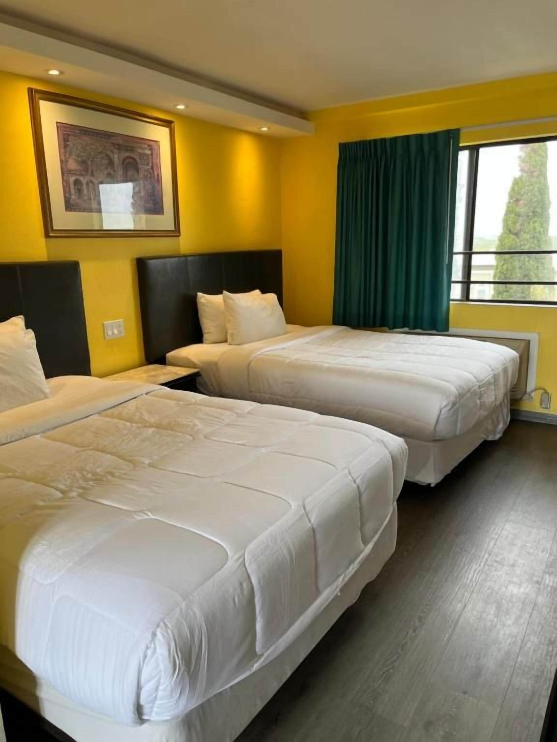 A hotel room with two beds, a framed picture on the wall, and a window with curtains.