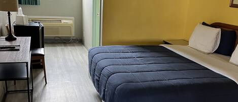 A hotel room with a bed, a desk, a chair, a lamp, and a window with curtains.