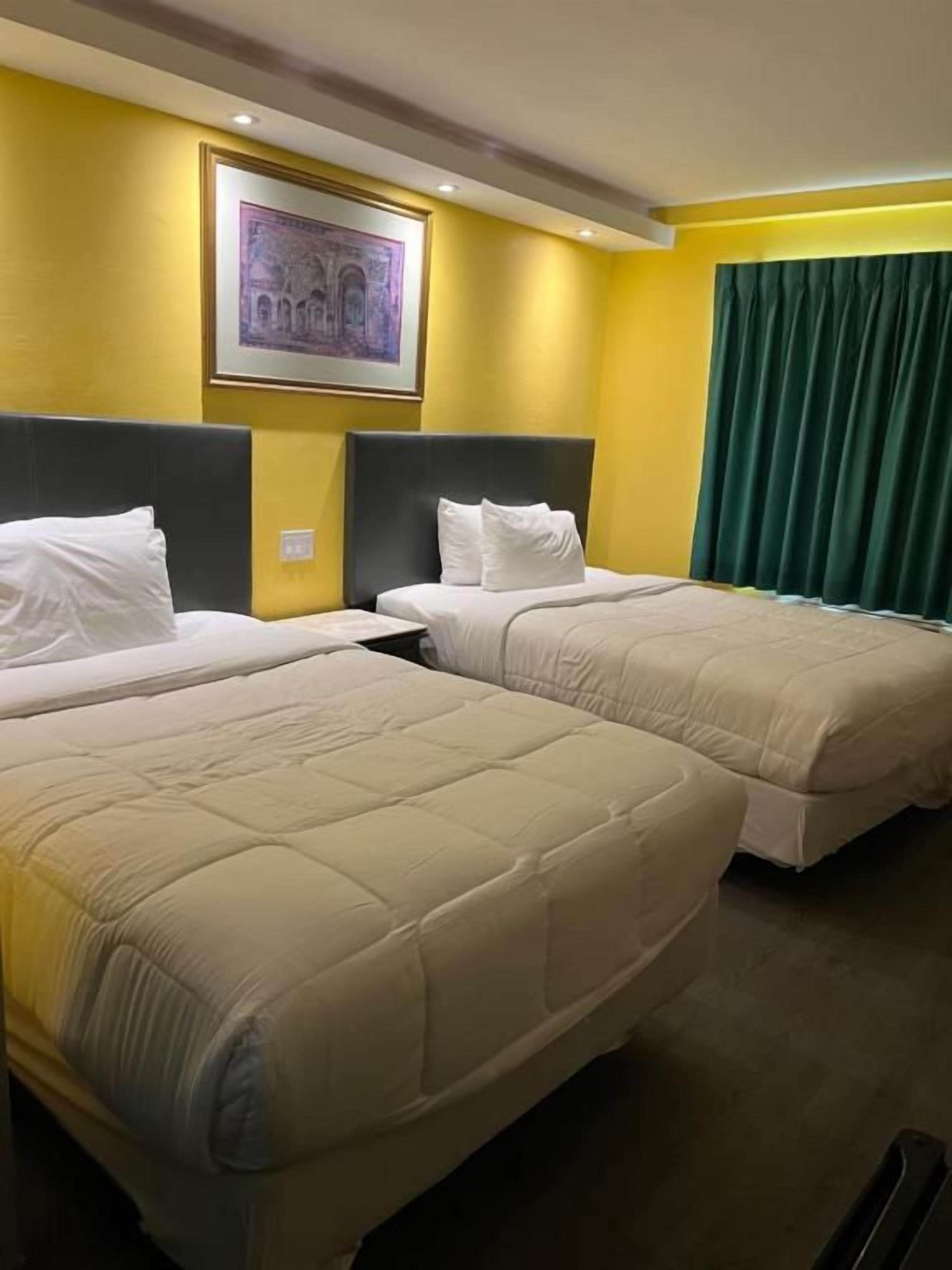 A hotel room with two beds, a framed picture on the wall, and a green curtain.