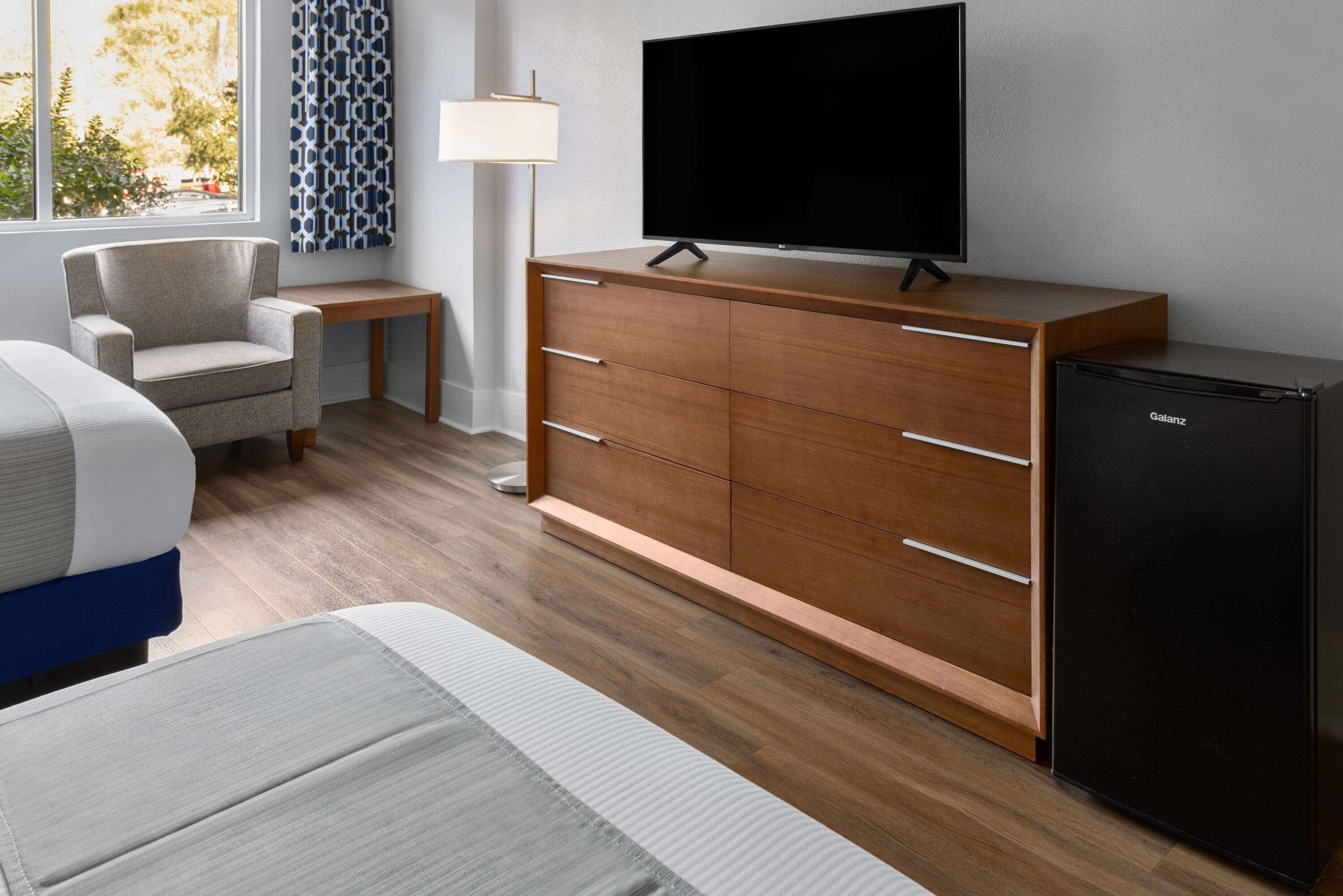 Una habitación de hotel moderna con un aparador de madera, un televisor de pantalla plana, una mesita y una silla.